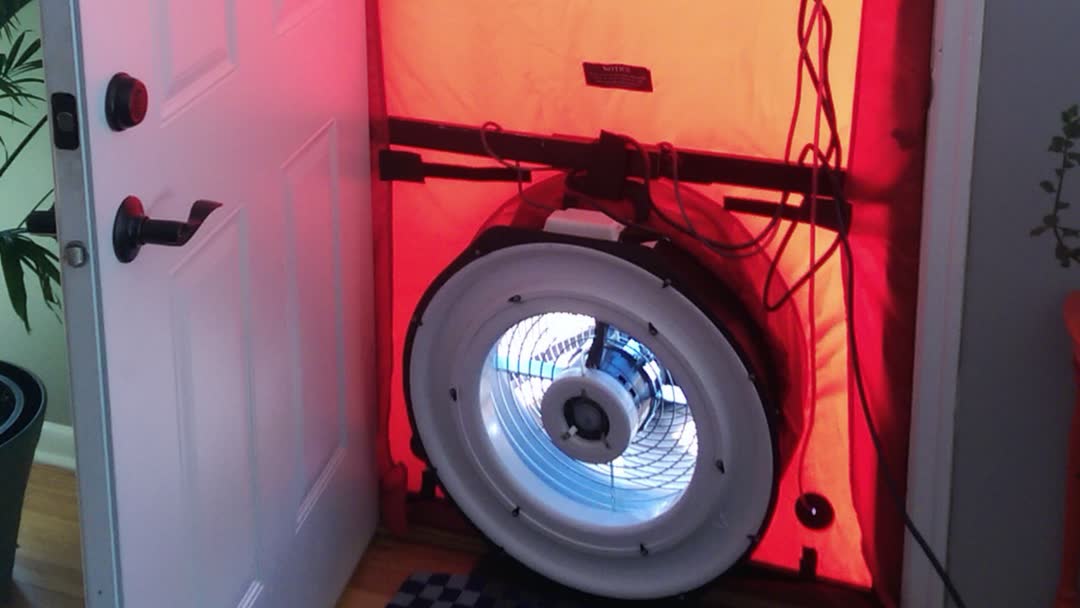 A blower door test set up in a front doorway: a red fabric panel seals the opening around a large round fan.