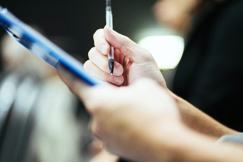 A hand holding a pen over a blue clipboard.