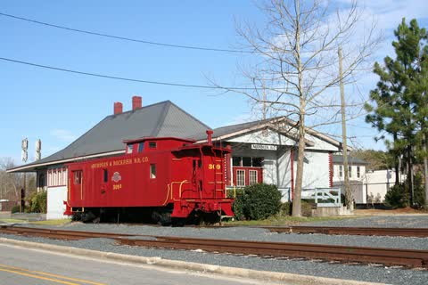 Red caboose on a track in front of the white Aberdeen train station