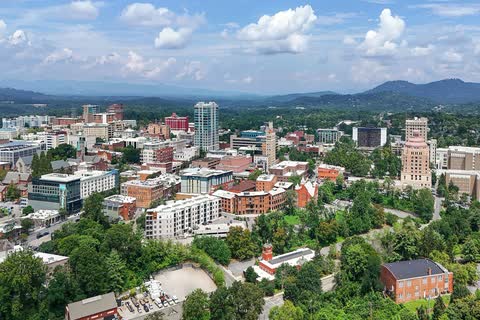 Aerial view of downtown Asheville buildings and trees with blue mountain ridges on the horizon