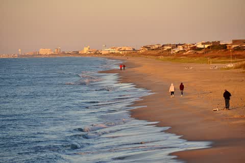 Waves washing up on a wide sandy beach in warm evening light at Atlantic Beach, with a few distant walkers