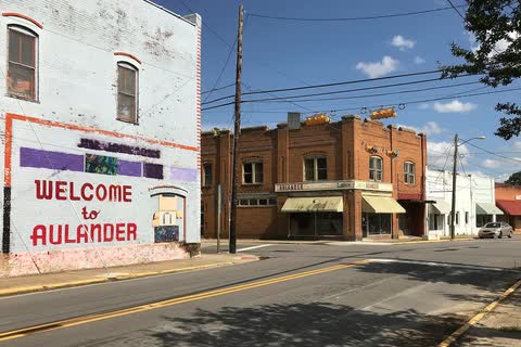 A painted 'Welcome to Aulander' wall beside a downtown street with brick commercial buildings