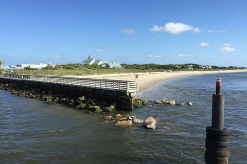 A rock jetty and channel marker at the Bald Head Island harbor entrance, with the beach and dunes behind