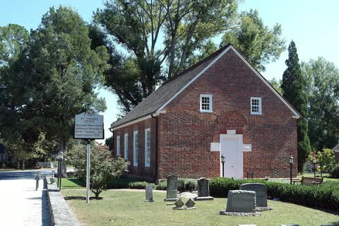 A small red-brick colonial church among trees and old gravestones in Bath