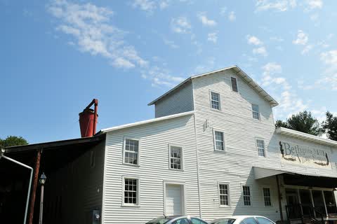 The Bethania Mill, a large white clapboard building with a red metal chute on the roof, under a blue sky