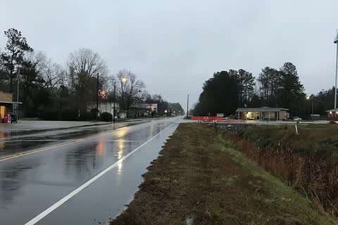 A wet two-lane highway through Bolton with the post office at left and the town water tower at right