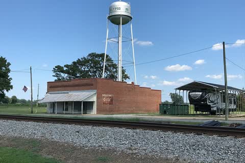 A brick building beside railroad tracks with the town water tower behind it in Calypso