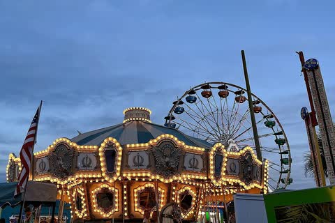 A lit carousel and a Ferris wheel at the Carolina Beach Boardwalk amusement park at dusk