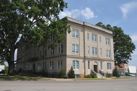 Three-story stone courthouse among large shade trees in Carthage