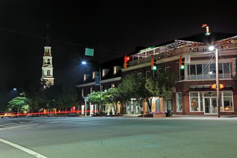 Lit storefronts on Franklin Street in Chapel Hill at night, with a white church steeple on the left