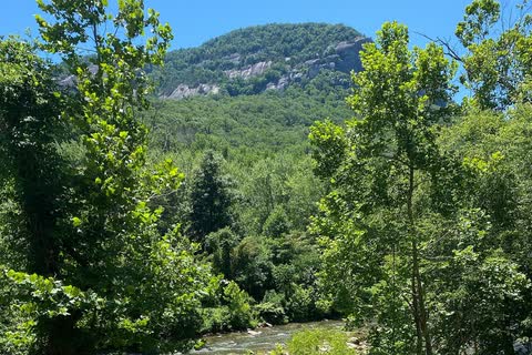 The wooded cliffs and summit of Chimney Rock seen from Chimney Rock Village, above the river