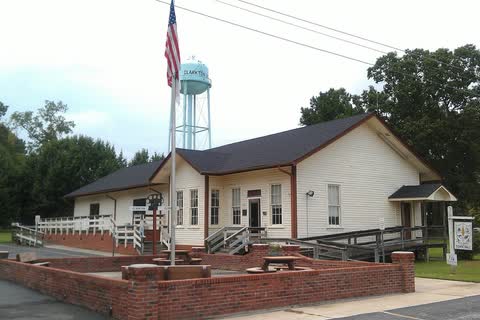 A restored white wooden railroad depot with a flagpole and the town water tower behind it in Clarkton