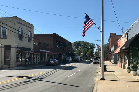 Brick storefronts along East Main Street in downtown Clayton, with an American flag on a light pole