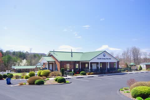 Brick town hall with a green metal roof and landscaped parking area in Connelly Springs