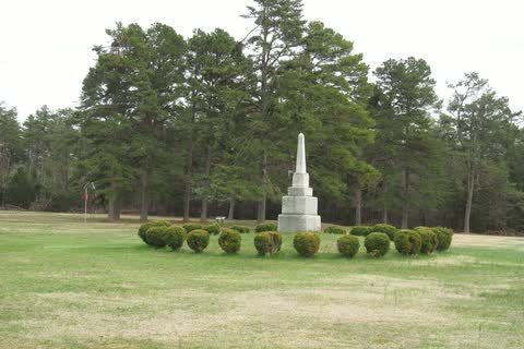 Stone monument on an open field ringed by tall pine trees