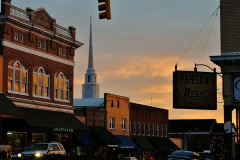 Historic brick buildings and a white church steeple against an orange evening sky in Wadesboro