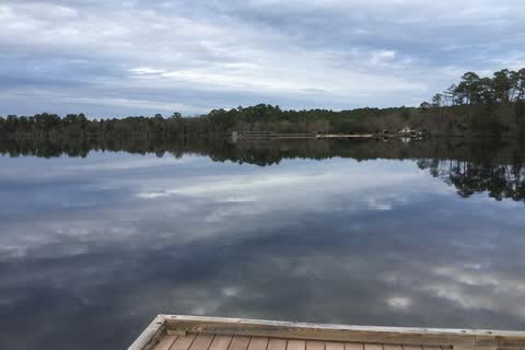 Calm lake water reflecting clouds, seen from the end of a wooden pier