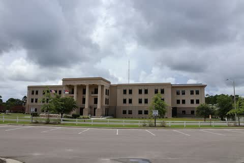 A long tan courthouse with a columned center behind a parking lot