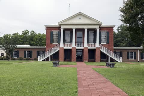 Red-brick courthouse with white columns, twin outdoor stairways and the date 1847 in its pediment, behind a brick walk