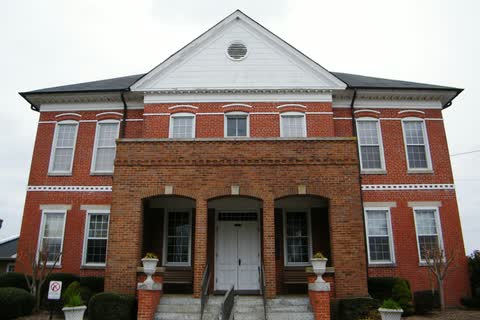 Two-story red-brick courthouse with an arched brick entrance porch and a white gable