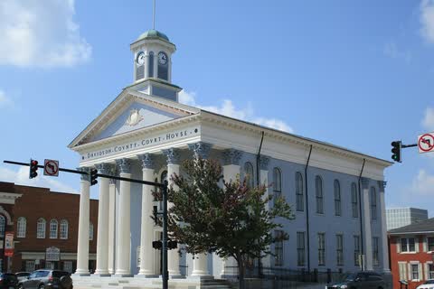 White temple-front courthouse with tall columns and a cupola beside a street