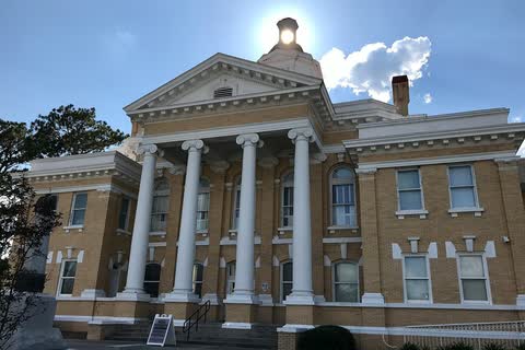 A tan-brick courthouse with tall white columns, the sun behind its cupola, in Kenansville