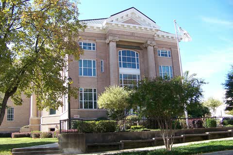 Tan neoclassical courthouse with columns and trees in front in Gastonia