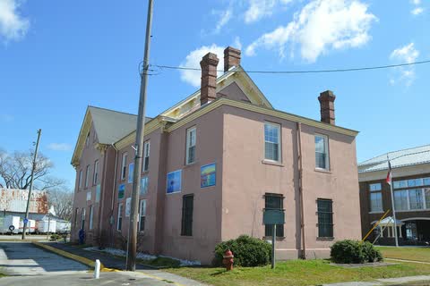 Two-story pink stucco courthouse with brick chimneys and a historical marker, the newer brick courthouse at right
