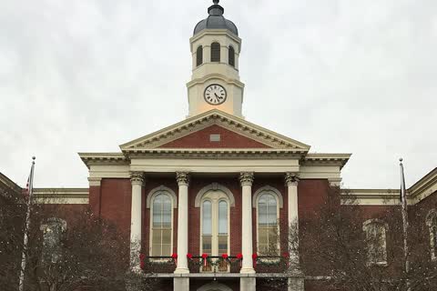 Red-brick courthouse with white columns, a pediment dated 1882 and a clock tower, hung with holiday wreaths