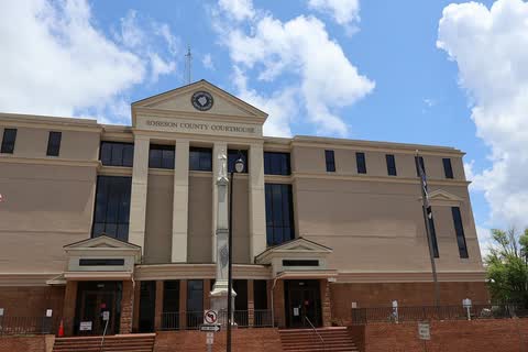 Tan multi-story courthouse with a pedimented entrance under a cloudy blue sky