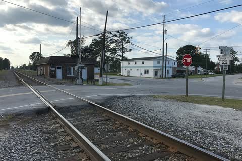 Railroad tracks crossing a road beside small buildings in Cove City