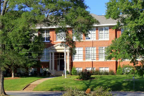 Two-story red brick Mayworth School building with white trim behind large shade trees in Cramerton