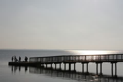 The boardwalk at Duck Town Park in Duck, a wooden pier over calm sound water with a few people in silhouette