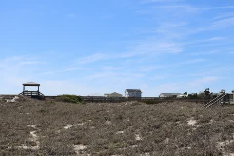 Grassy sand dunes and a beach-access walkway under a blue sky in Emerald Isle
