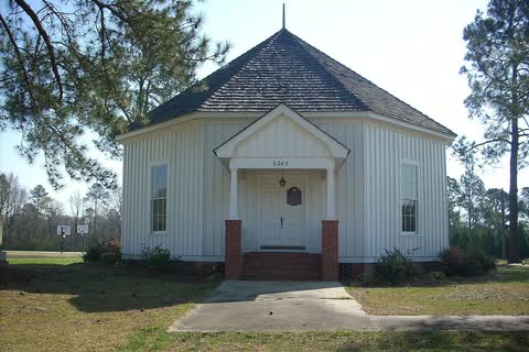 A white wooden eight-sided tabernacle building on a lawn among pines in Falcon