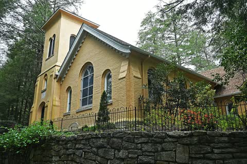 Yellow stucco St. John in the Wilderness church behind a stone wall and iron fence in Flat Rock