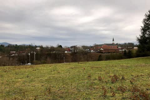 Rooftops and church steeple of downtown Franklin beyond a grassy field with mountains behind