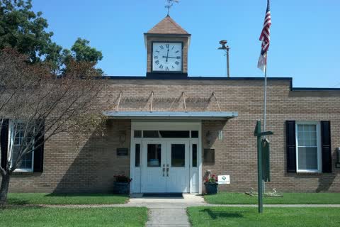 A one-story brick town hall with a white clock cupola and a flagpole in Hamilton