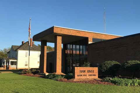 Modern brick municipal building with a flat canopy and a Haw River sign