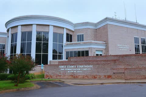 A modern courthouse with a curved glass front behind a brick wall in Henderson