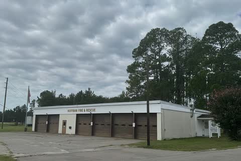 The Hoffman town hall and fire station, a long white building with garage bays under tall pine trees
