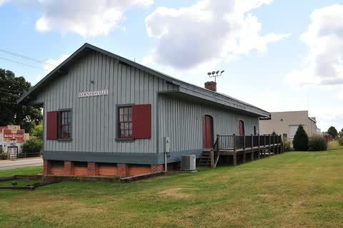 Gray wooden railroad depot with red shutters on a grassy lot in Kernersville