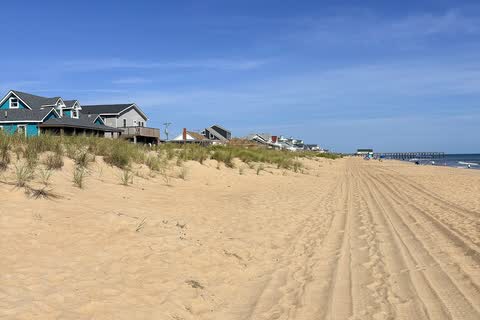 A wide sandy beach with dunes and beach houses stretching north at Kitty Hawk