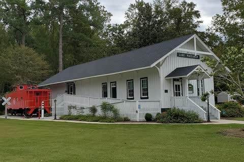 A white wooden railroad depot with a red caboose on its lawn in Lake Waccamaw