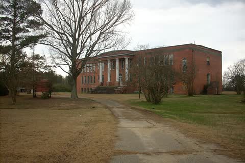 A large brick school building with a columned entrance at the end of a dirt lane in Linden