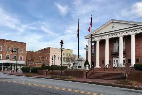 A red-brick courthouse with a white-columned portico beside downtown buildings in Louisburg