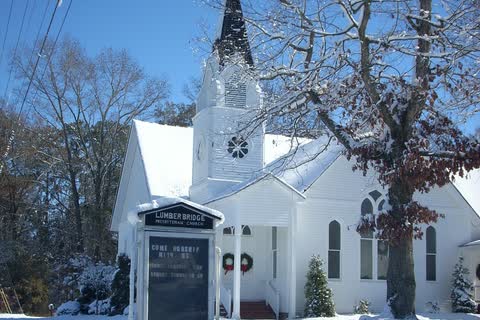 Lumber Bridge Presbyterian Church, white with a tall steeple, surrounded by snow