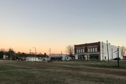 A low row of buildings across an open field in Macon at dusk