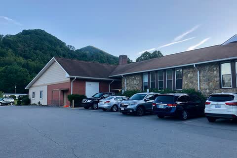 Low brick and stone former school building that houses Maggie Valley Town Hall, with mountains behind