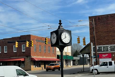 Town clock on a post in front of brick buildings in downtown Maiden